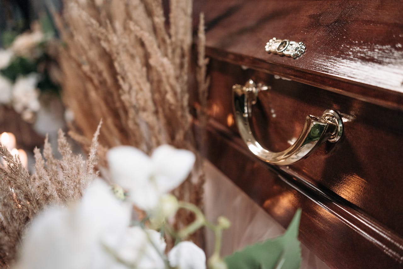 Close-up of a polished wooden casket adorned with floral arrangements, symbolizing loss and remembrance.